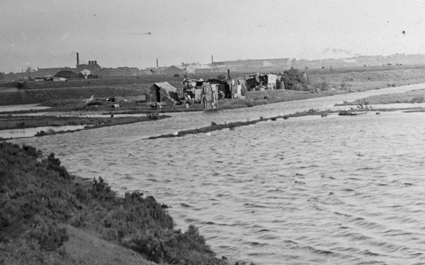 Black and white photo of a row of shacks made out of rubbish on the edge of the West Melbourne swamp