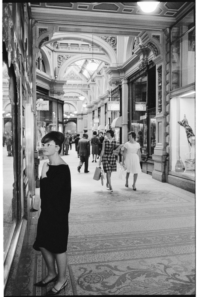 Glamorous brunette woman in black shift dress, 1950s style glasses and beehive hair looking in shop window, The Block Arcade, Melbourne.