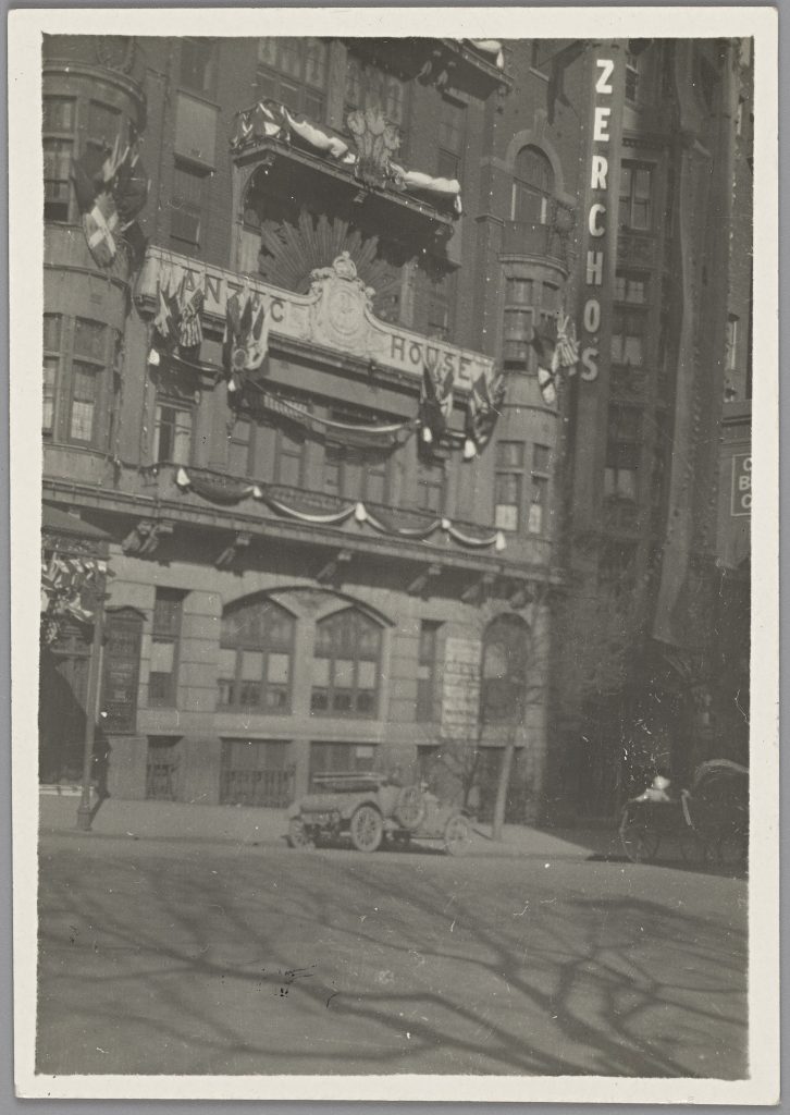 Black and white photograph of the front of Anzac House, decorated with flags, bunting and royal insignia. Zercho's business college (sign) next door.