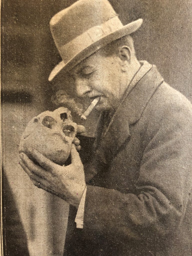 photograph of Detective Piggott holding a human skull and smoking a cigar
