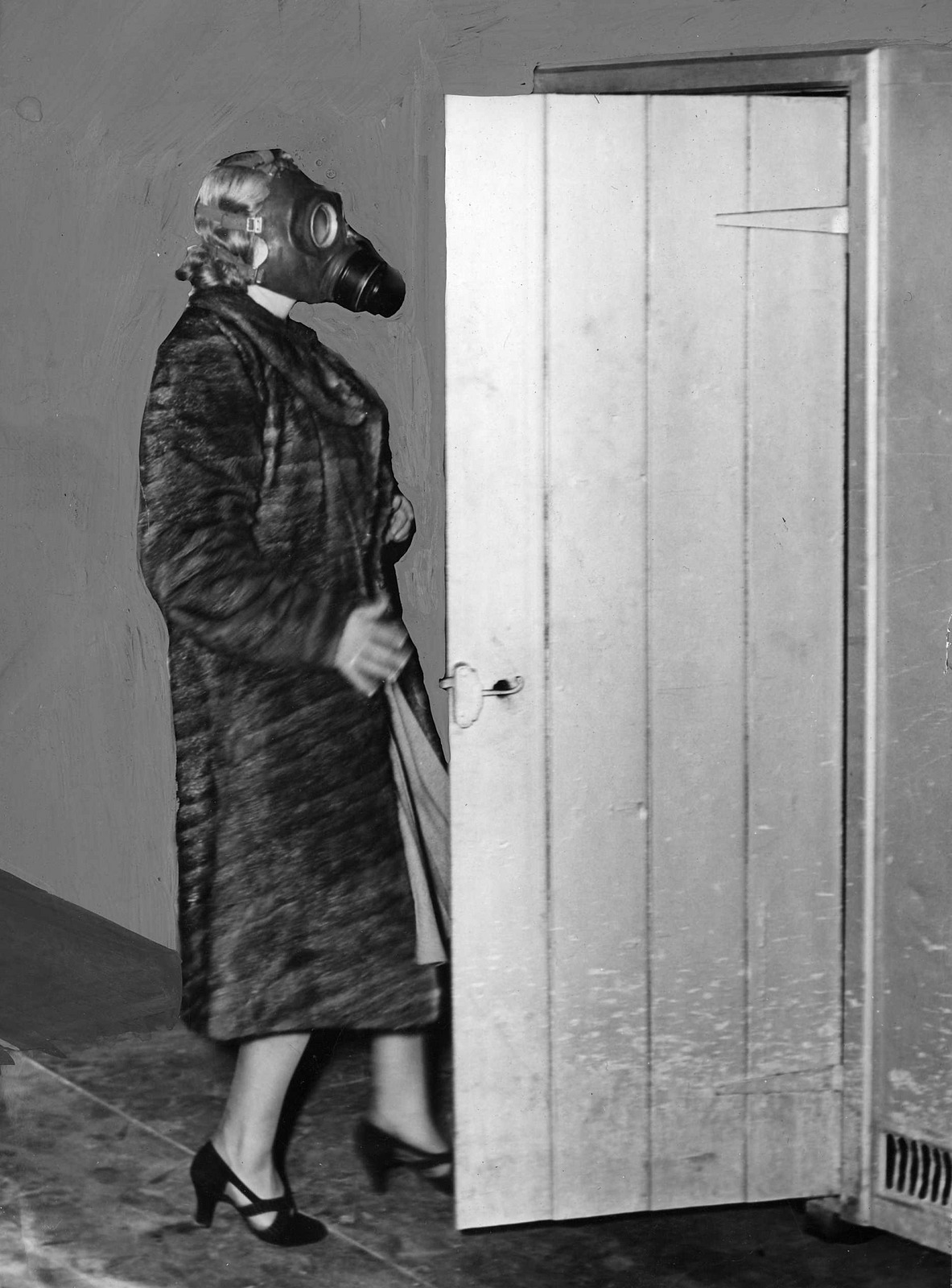 Shows woman in fur coat, wearing gas mask walking through doorway to another room.