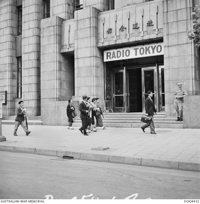 American soldiers and Japanese civilians in the street outside the entrance to the Radio Tokyo building.