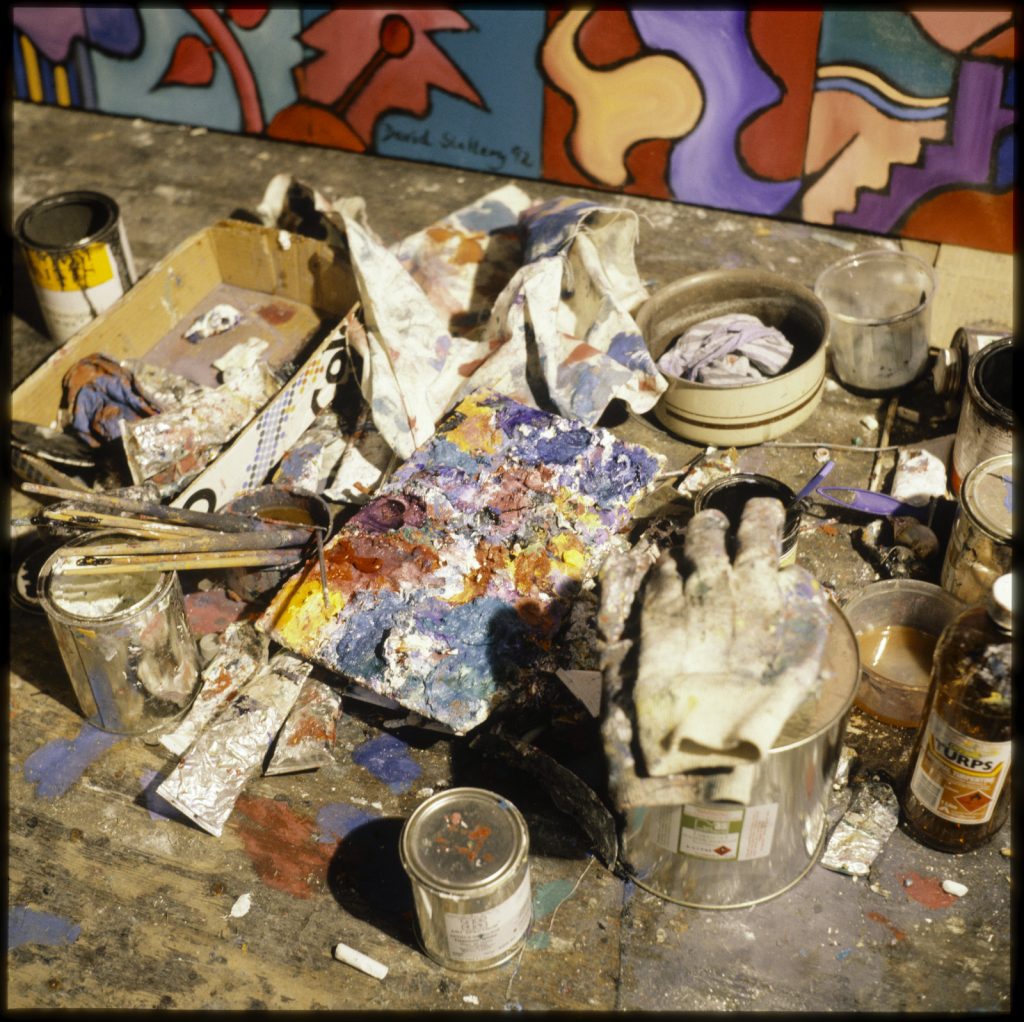 A photo of the material used by David Slattery to create his artwork including large cans of paint, gloves, and rags.