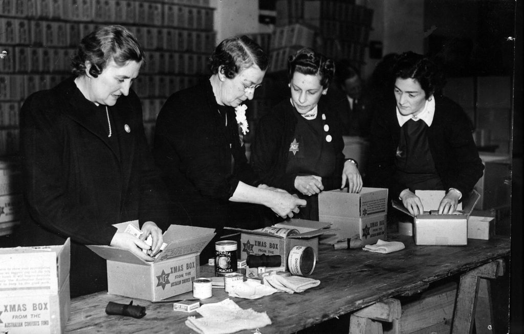 Black and white photo depicting women packing cans in boxes.