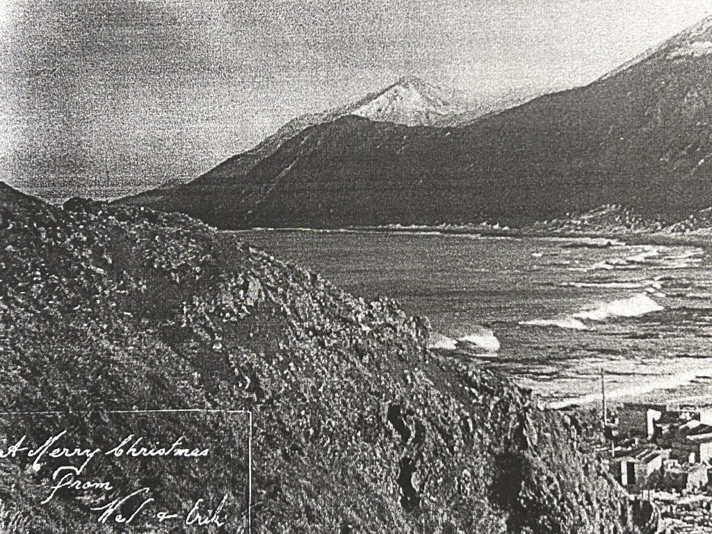 Black and white photo of the sea surrounded by mountains and small buildings far below.