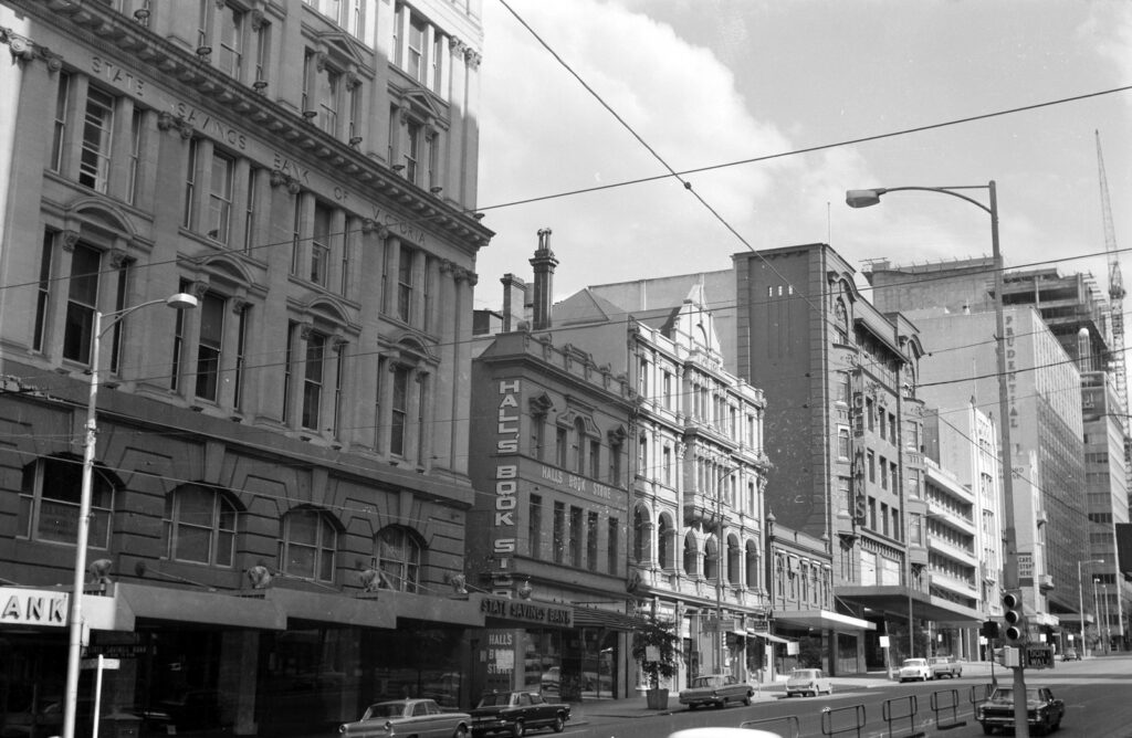 View of shopfronts on southern end of Bourke Street, including Hall's Book Store and signage.