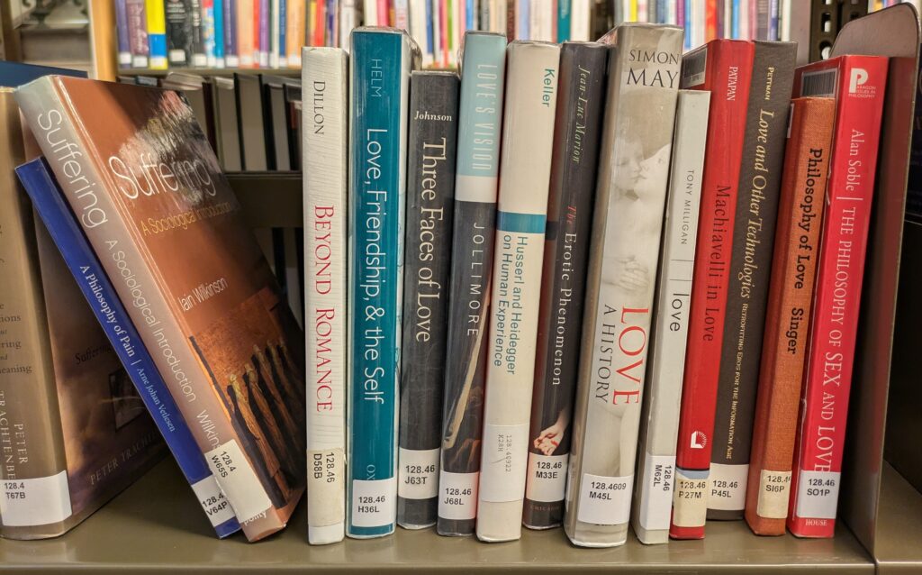 Photograph of a range of books on a library shelf, all about Love, next to a few books about suffering and pain. 