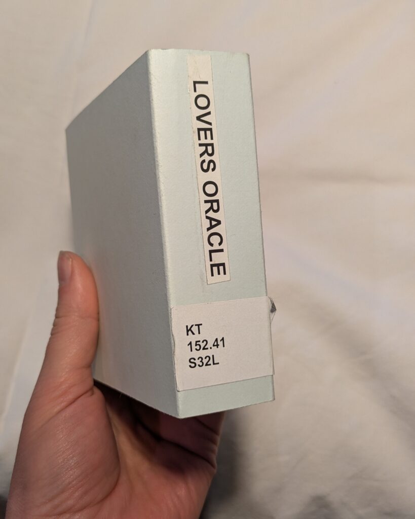 Photograph of a hand holding a small archival box reading "lovers oracle"