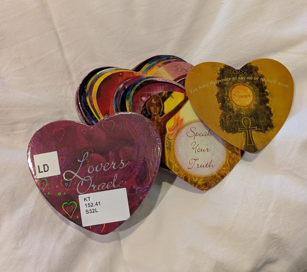 Photograph of an open heart-shaped tin box containing heart-shaped illustrated oracle cards. 