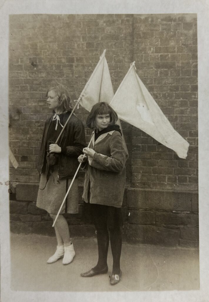 Photograph of two young women at a demonstration, carrying peace flags.
