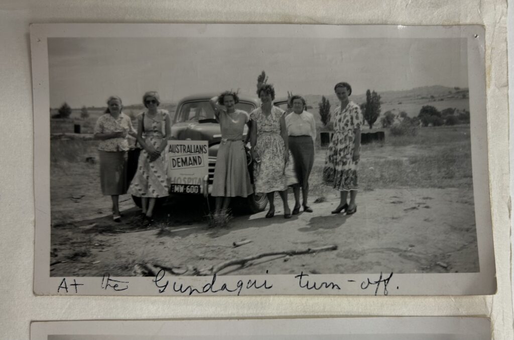 Photograph of six women standing in front of a car, with sign that reads: Australians Demand Hospitals.