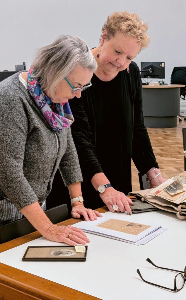Coloured photo showing two women standing over a table, looking at some photocopied images.